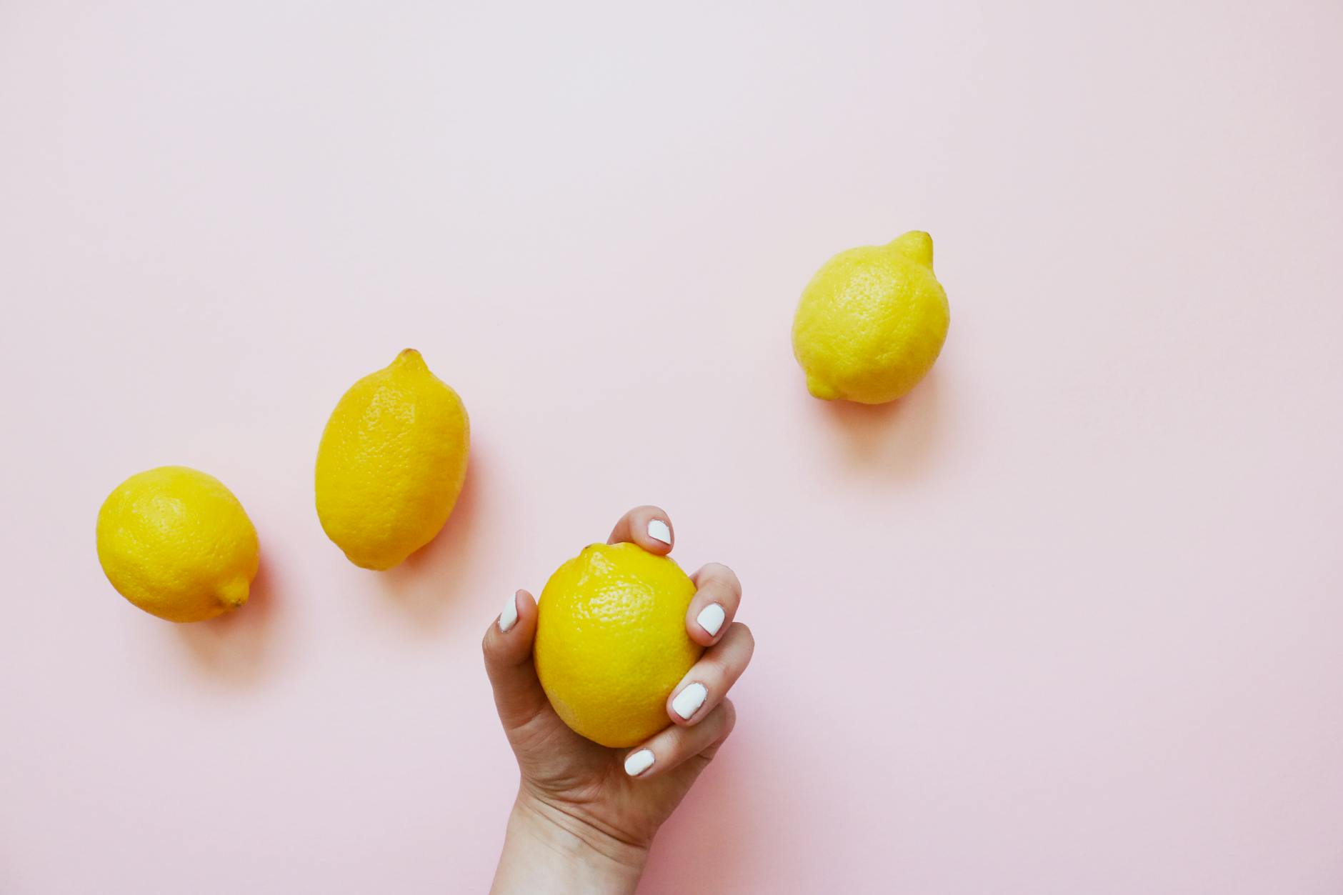 A hand holding a bright lemon on a soft pink background, symbolizing quick and natural pleasure