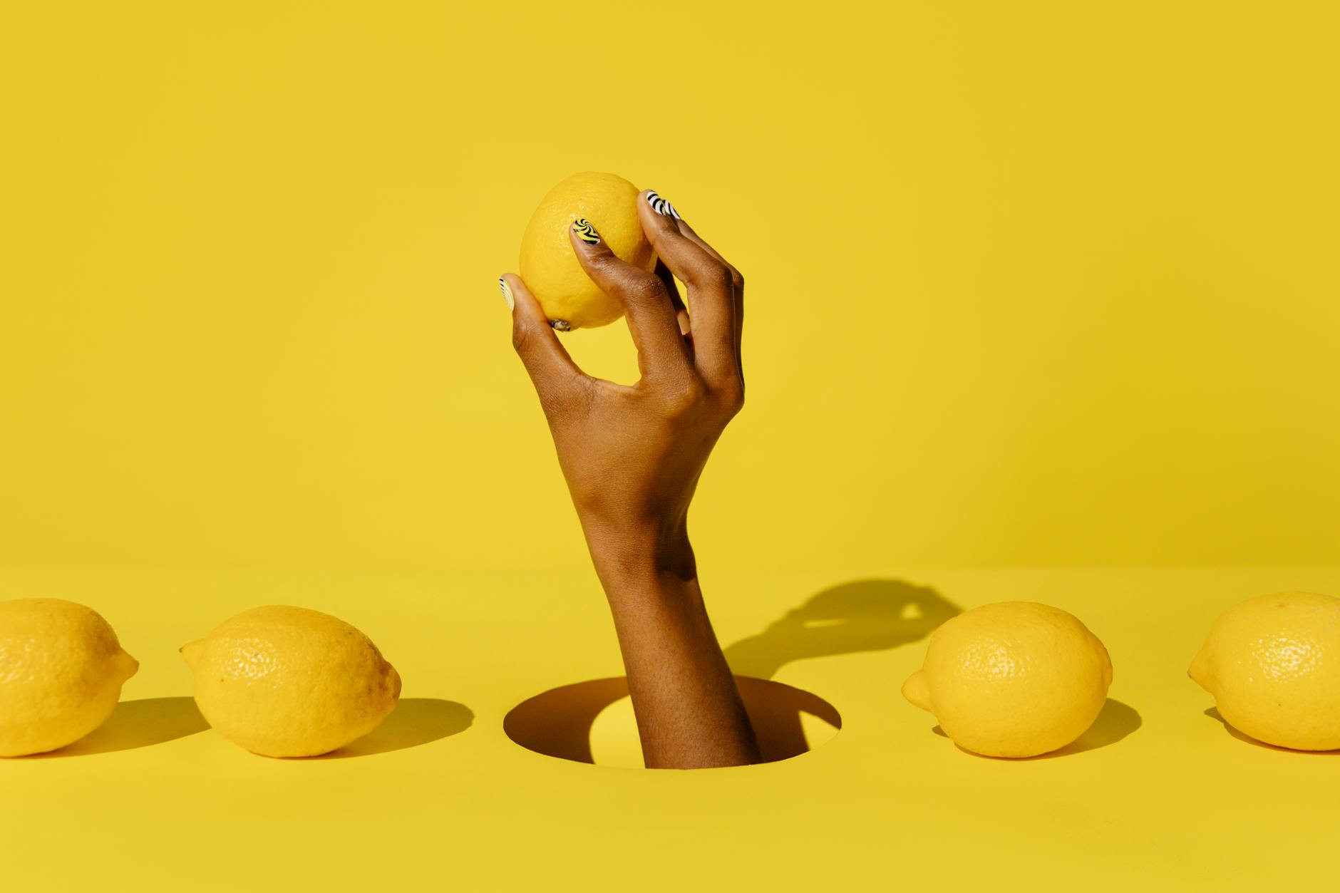 A hand holding a lemon against a vibrant yellow background, representing fresh and intentional pleasure