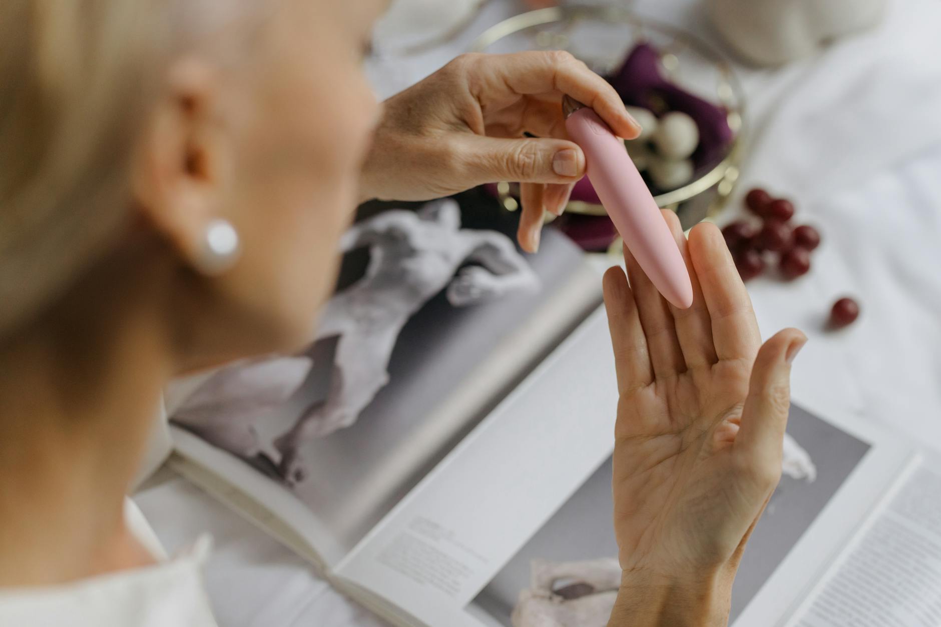 Close-up of a woman holding a pink vibrator with art books in the background, symbolizing intimacy and personal empowerment