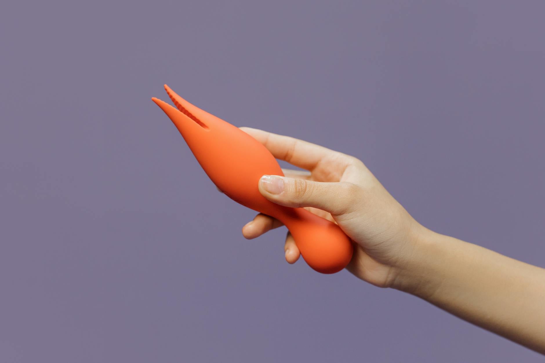 Hand holding a lemon-shaped vibrator against a purple backdrop