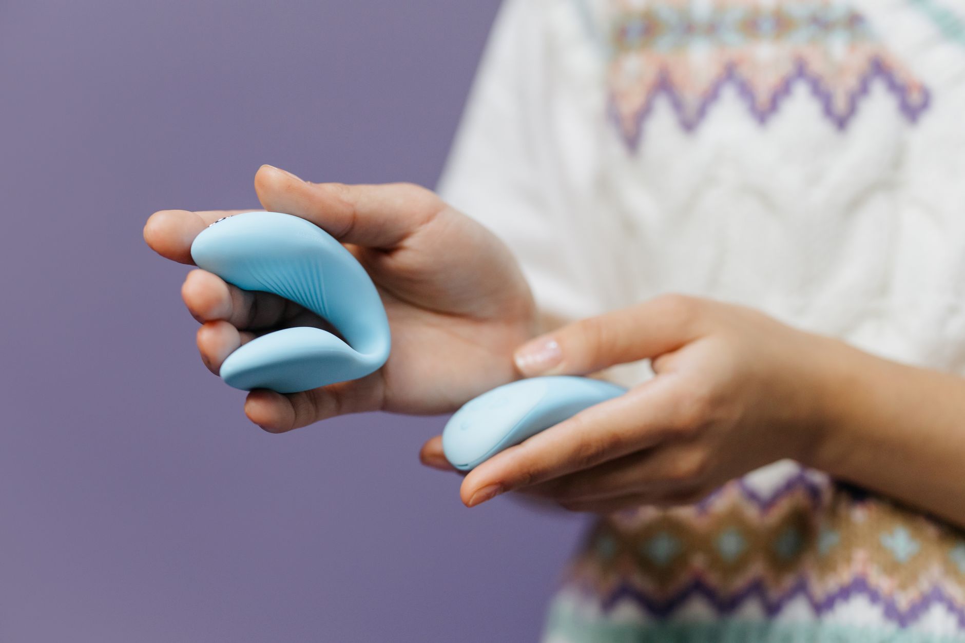 Hand holding a sleek blue lemon vibrator against a purple background, ready to use