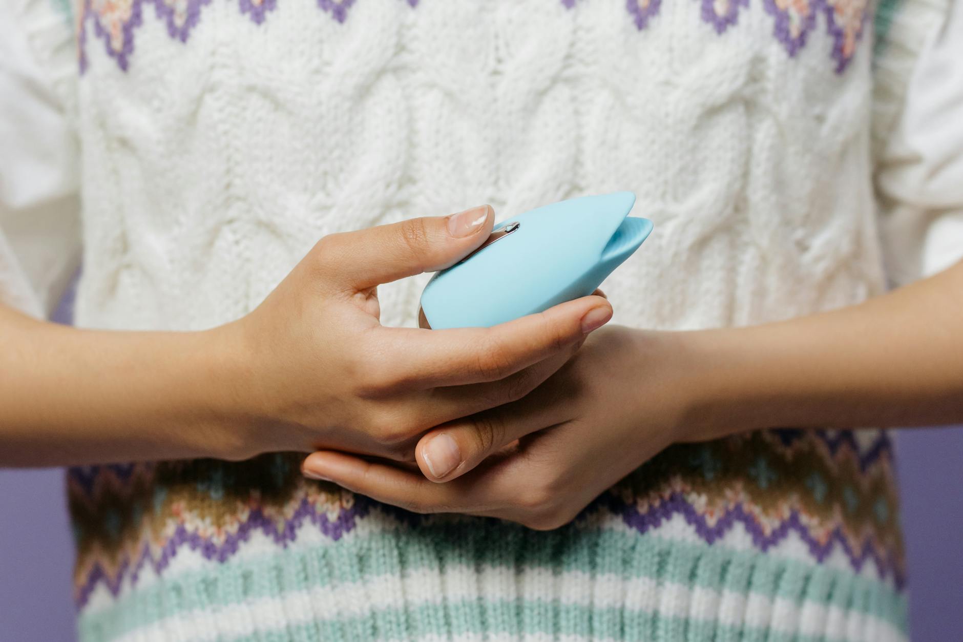 Close-up of a blue silicone clitoral vibrator held in hand against a soft purple background
