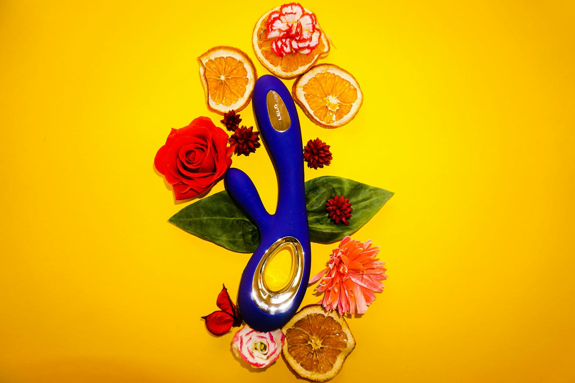A blue lemon-shaped vibrator surrounded by flowers and citrus slices on a yellow background