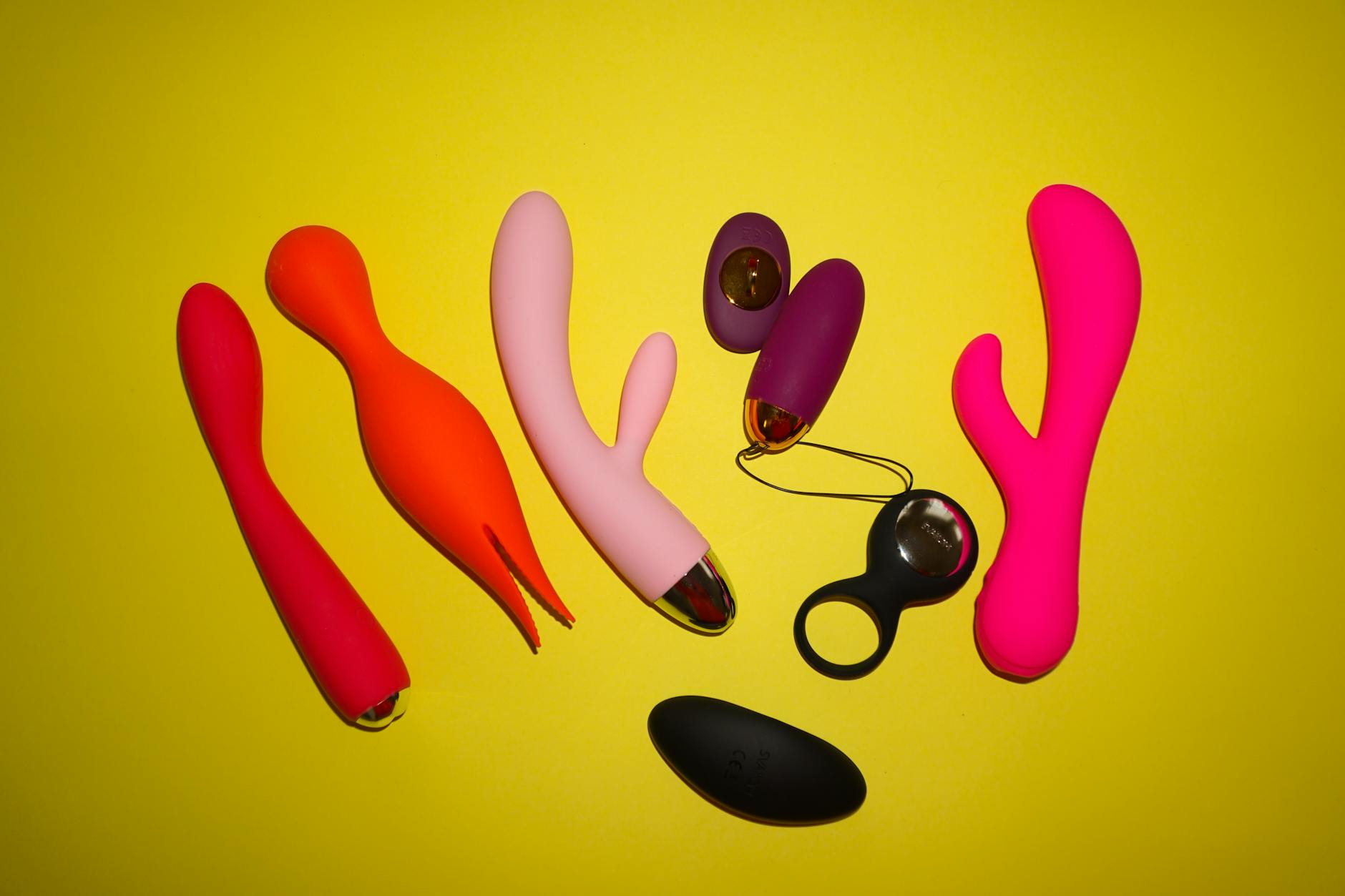 Woman with eyeglasses holding blue and pink silicone vibrators in a contemplative manner